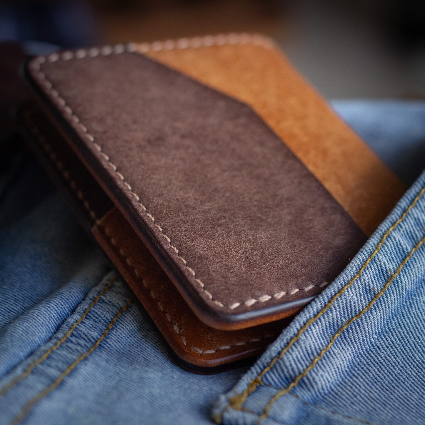The cred brown bifold handmade leather wallet on top of blue jean pocket reverse quick access pocket