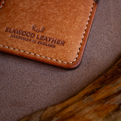 LEATHER TEMPLATE - Elkwood Leather - The Maple - minimalist full grain Italian Pueblo leather cardholder wallet close up of handstitched edges on roll of leather next to wood grain