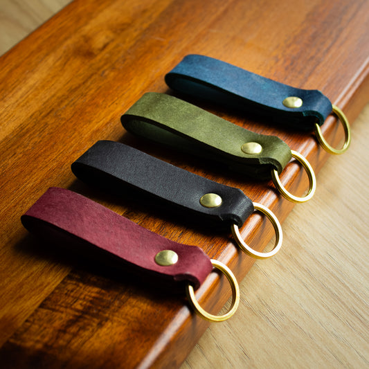 handmade leather keytags with solid brass keyring and rivet on top of wooden chopping board - Made from Peublo leather - blue, black, green, red