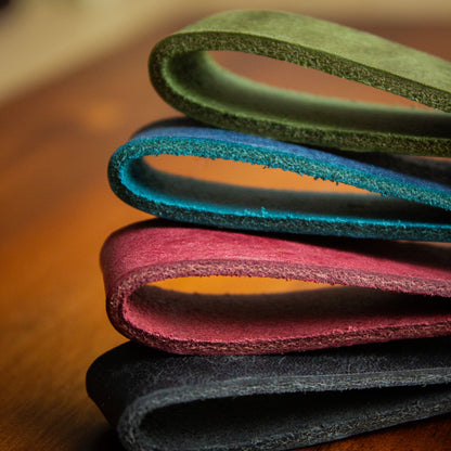 handmade leather keytags with solid brass keyring and rivet on top of wooden chopping board - Made from Peublo leather - blue, black, green, red - close up key loops