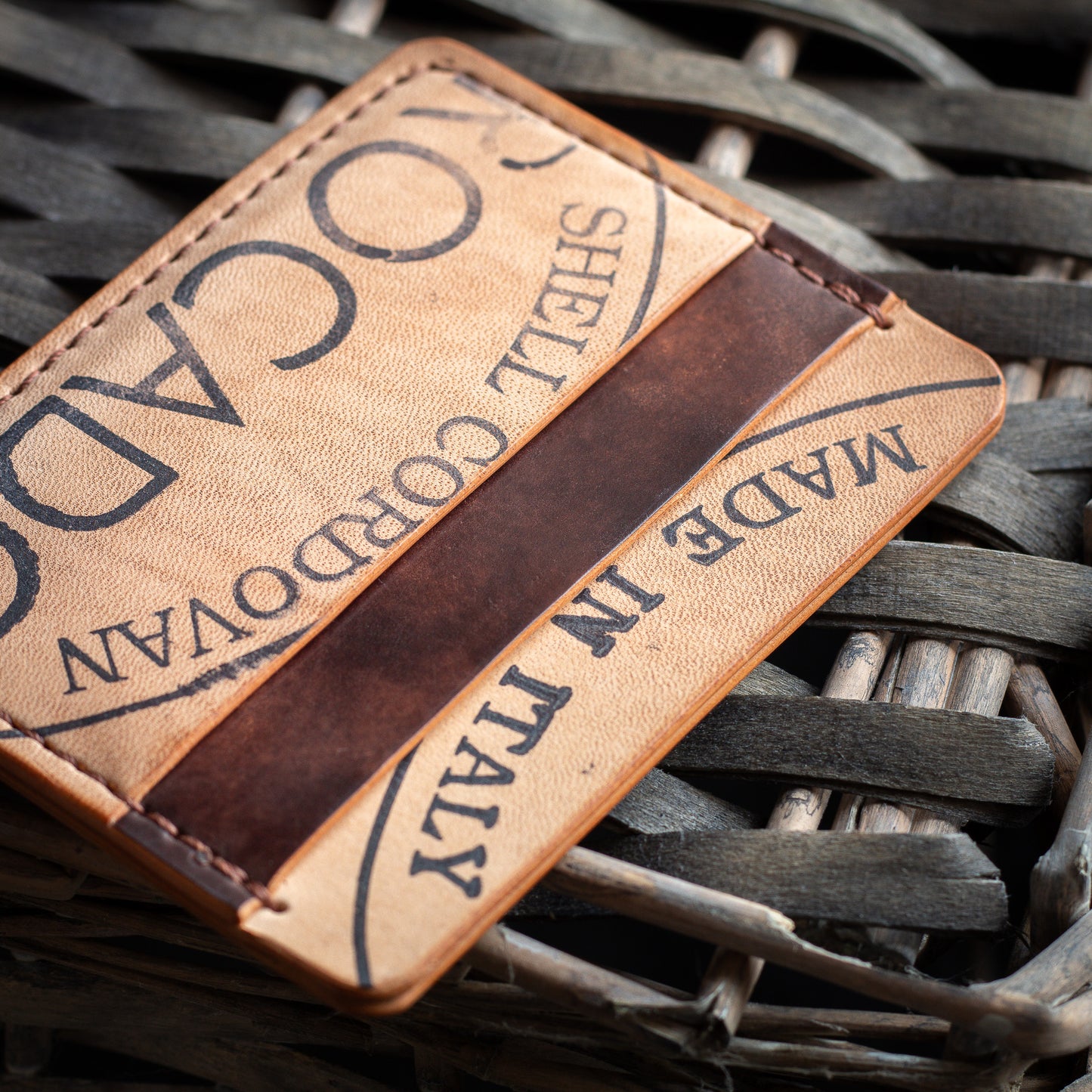 reverse shell cordovan leather wallet - brown museum Rocado shell cordovan leather onto of whicker basket - featuring Rocado Shell Cordovan made in Italy logo - close up of pockets and stitching