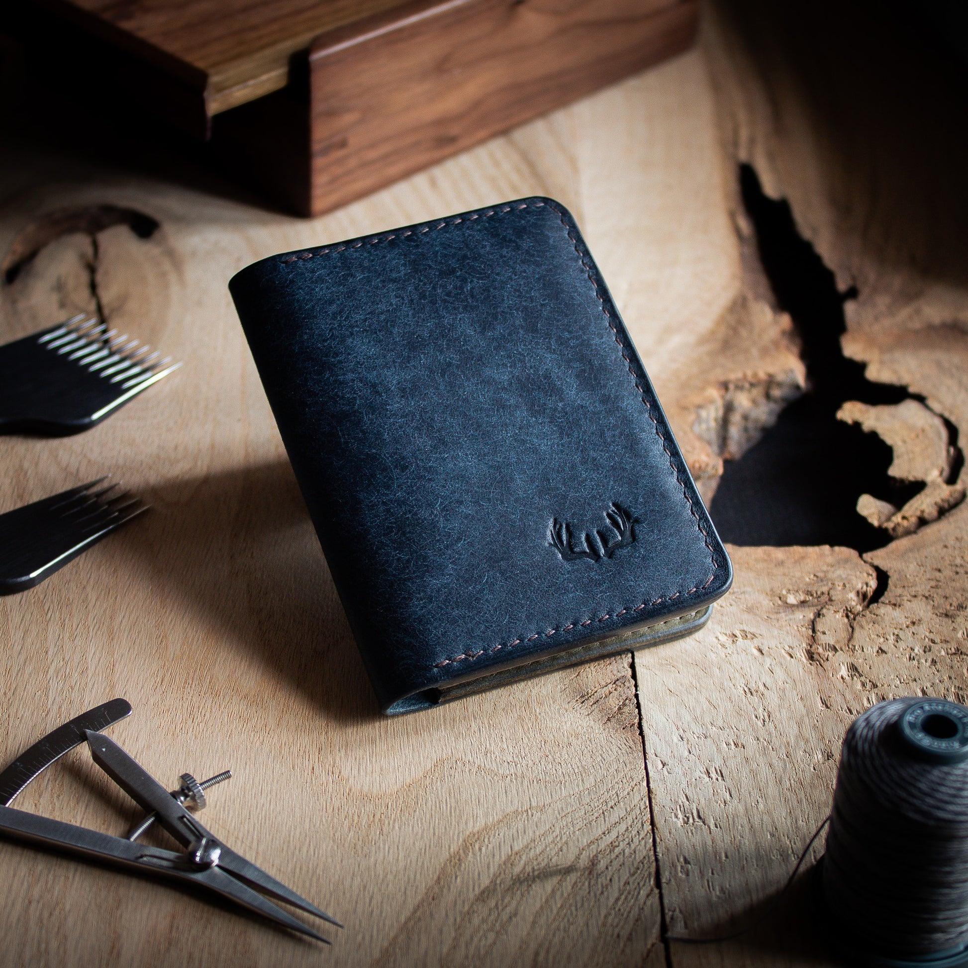  handcrafted Navy leather wallet with antlers logo, surrounded by leathercraft tools on wooden table closed