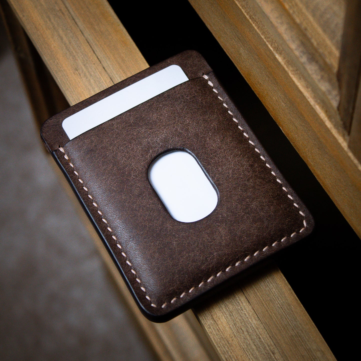 Brown leather cardholder with quick access slot on top of wooden dresser
