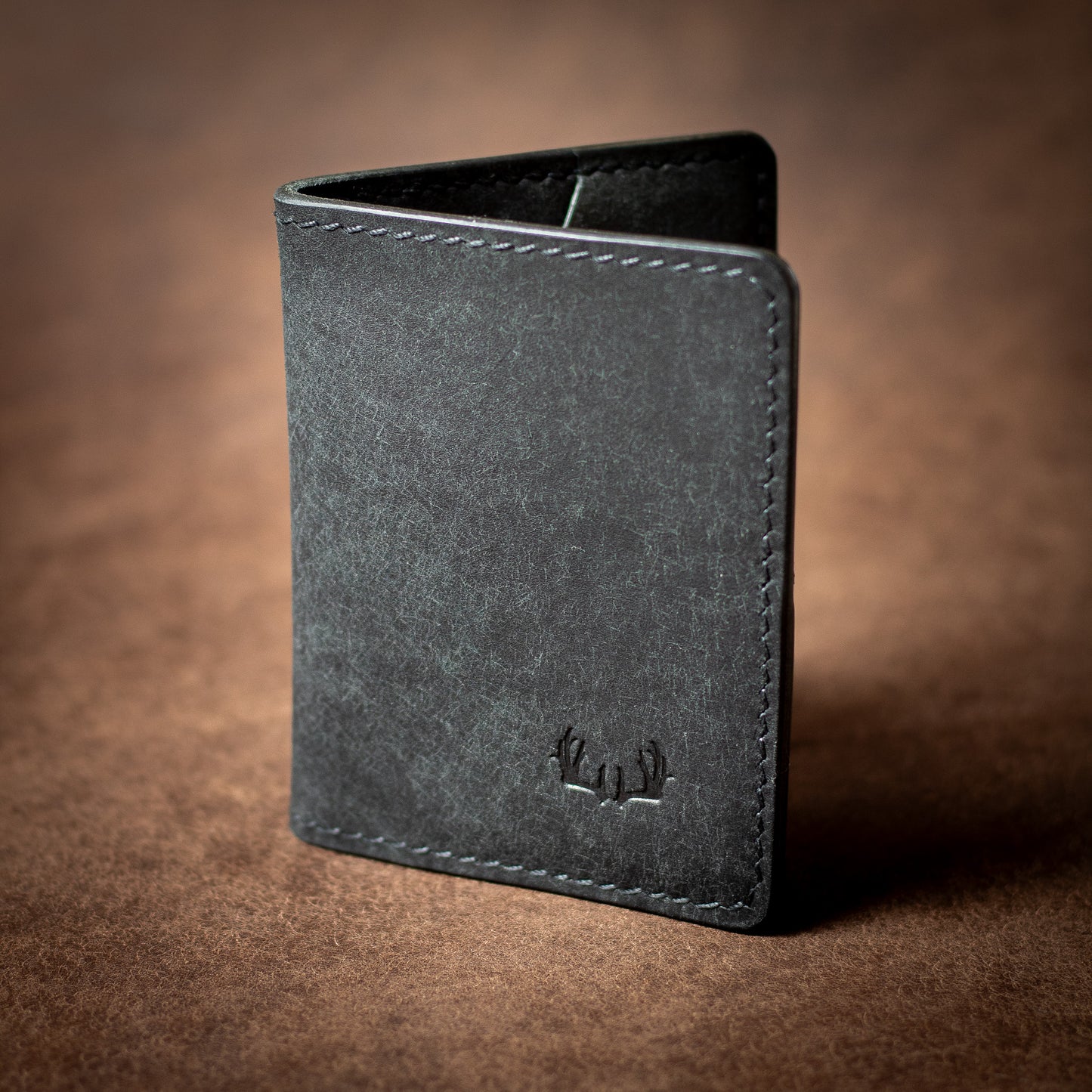 Elkwood Leather black leather bifold wallet with black stitching on a brown leather background closed