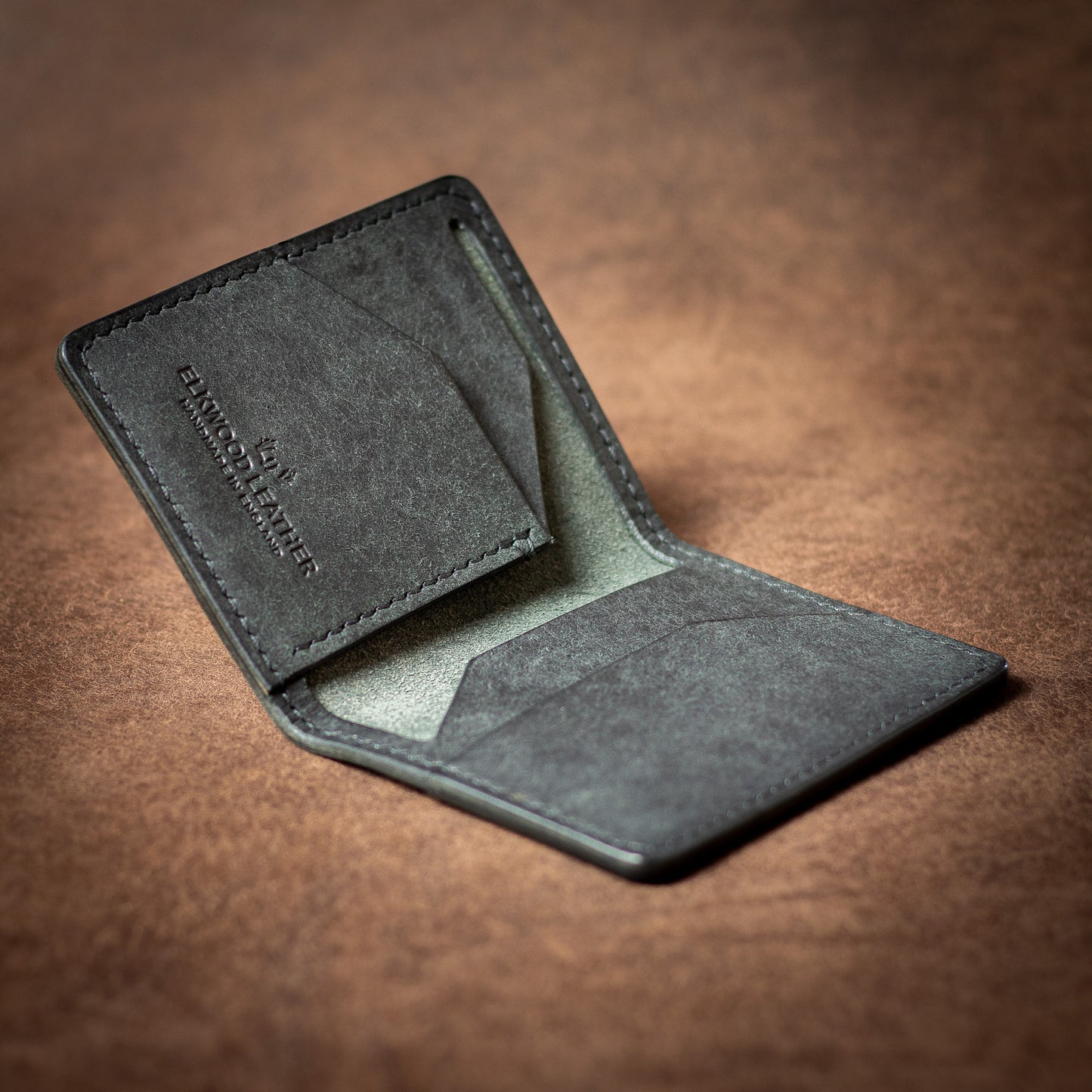 Elkwood Leather black Italian leather bifold wallet with black stitching on a brown leather background open