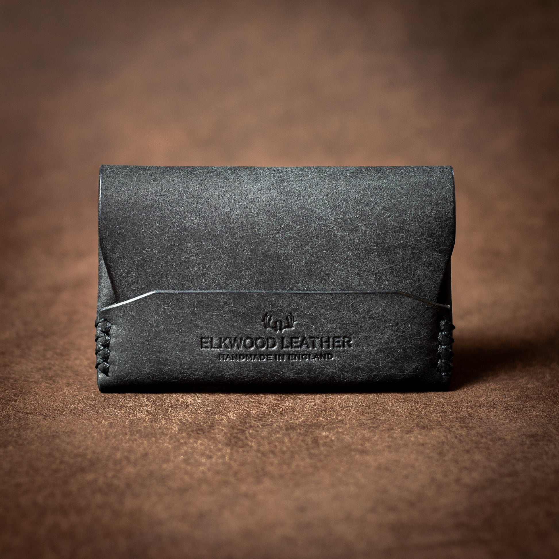 Elkwood Leather black leather EDC flap wallet with black stitching on a brown leather background closed