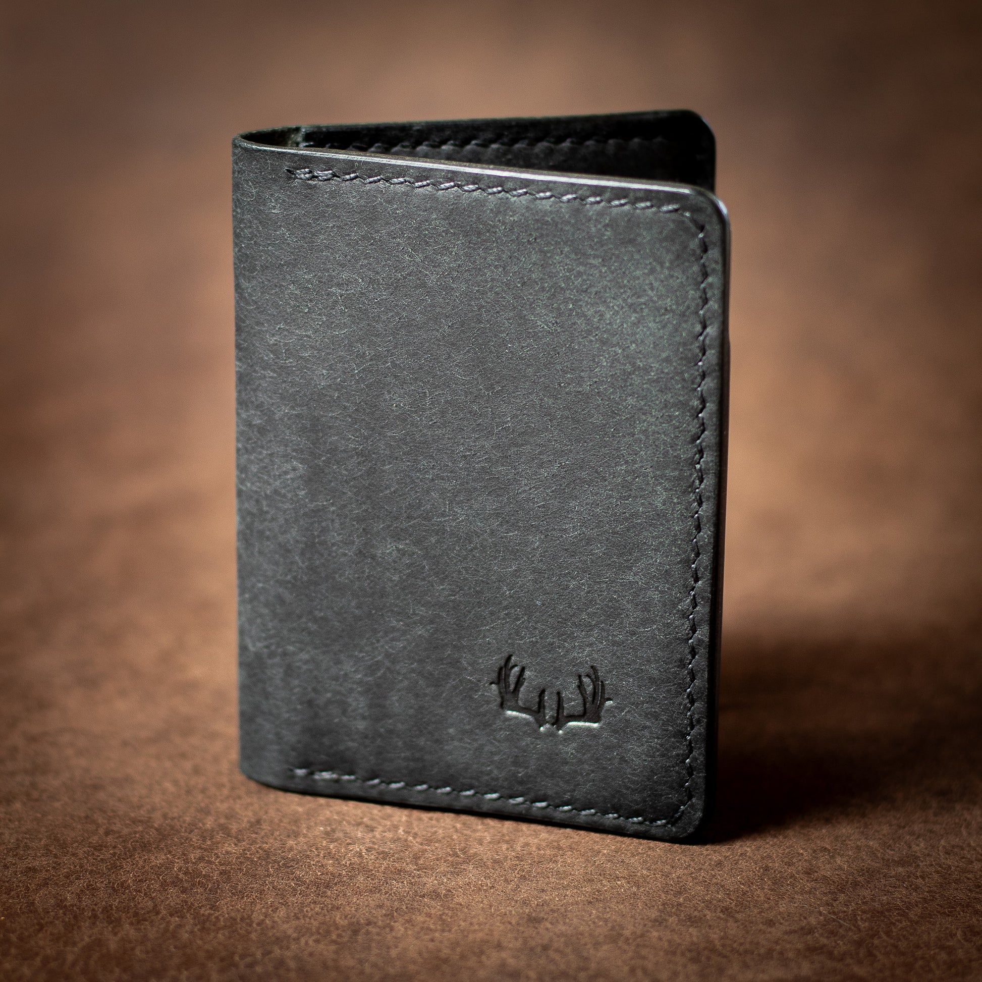 Elkwood Leather black leather bifold cardholder wallet with black stitching on a brown leather background closed