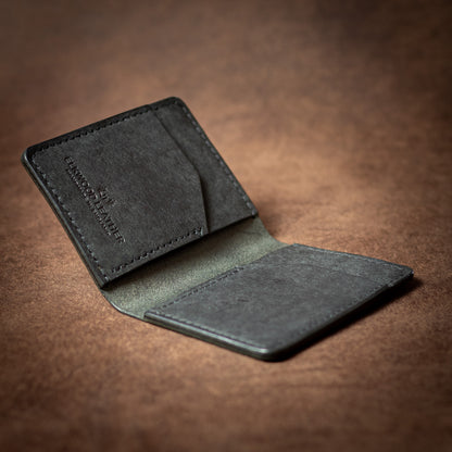 Elkwood Leather black leather bifold cardholder wallet with black stitching on a brown leather background open